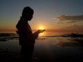 Silhouette of a young girl with sun arise in hands on the sea. Background of a person with sunset sunrise in hand on beach