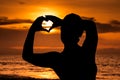 Silhouette of young girl with sunset on the beach, forming the shape of a heart with hands. Royalty Free Stock Photo