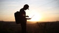 Silhouette of young guy on a hiking, using laptop for searching coordinates.