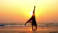 Silhouette of young gymnast woman doing handspring on sandy beach at sunset