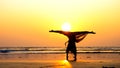 Silhouette of young gymnast woman doing handspring on sandy beach at sunset