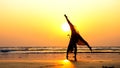 Silhouette of young gymnast woman doing handspring on sandy beach at sunset