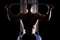 Silhouette of young handsome topless bodybuilder works out pulling down on cable machine in gym