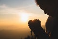 Silhouette of young human hands praying with a cross at sunrise, Christian Religion concept background