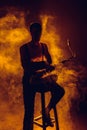 silhouette of young jazzman sitting on stool and holding saxophone