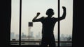 Silhouette of young man dancing ad listening music in wireles headphones stand on hotel room balcony