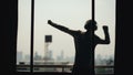 Silhouette of young man dancing ad listening music in wireles headphones stand on hotel room balcony