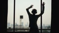 Silhouette of young man dancing ad listening music in wireles headphones stand on hotel room balcony