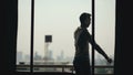 Silhouette of young man dancing ad listening music in wireles headphones stand on hotel room balcony