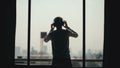Silhouette of young man dancing ad listening music in wireles headphones stand on hotel room balcony