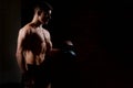 Silhouette of a young man doing weight exercises with a dumbbell on a dark background.