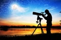 Silhouette of young man looking through a telescope