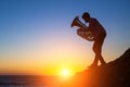 Silhouette of a young man playing the trumpet on rocky sea coast during sunset. Royalty Free Stock Photo