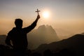 Silhouette of Young man praying and holding christian cross for worshipping God at sunset background. Christian Religion concept