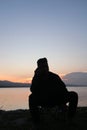 Silhouette of a young man sitting by the lake enjoying the sunset Royalty Free Stock Photo