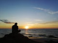 Silhouette of young man sitting on the rock while watching the sunset on the seaside Royalty Free Stock Photo