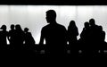 Silhouette of young man standing alone and a crowd of people walking behind him