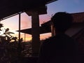 Silhouette of young man standing alone watching colorful sunset light over the top of house roof Royalty Free Stock Photo