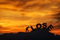 Silhouette of young man struggling to push a text of lose while climbing on the cliff , sky and sun light background. copy space