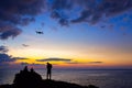 Silhouette of young man using and watching a flying drone in twilight sky over the sea for photos or video making Royalty Free Stock Photo