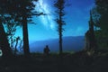 Silhouette of a young man who sits on the edge of the observation deck and enjoying night landscape with starry sky and full moon. Royalty Free Stock Photo