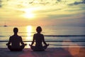 Silhouette of young man and woman practicing yoga in the lotus position on the ocean beach. Royalty Free Stock Photo