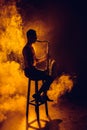 silhouette of young musician sitting on stool and playing saxophone