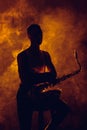 silhouette of young musician sitting on stool with saxophone