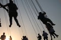 Silhouette of young people on Ferris wheel and swinging carousel in stop motion on sunset background