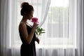 silhouette of a young sad woman in a dress with a peony in her hands on the background of a window, the concept of a Royalty Free Stock Photo