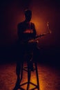 silhouette of young saxophonist sitting on stool