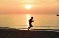 Silhouette young sport man running outdoors on beach at sunset with orange sky Royalty Free Stock Photo