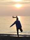 Silhouette young sport man stretching leg after running workout outdoors on beach at sunset Royalty Free Stock Photo