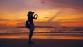 Silhouette of young tourist woman in hat taking photo with cellphone during sunset in ocean beach Royalty Free Stock Photo
