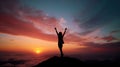 Silhouette of a young woman with arms raised on top of a mountain above the clouds at sunset or sunrise. Royalty Free Stock Photo
