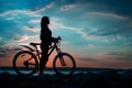 Young woman staying on the shore of the lake with bicycle at sun