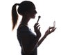 Silhouette of a young woman doing makeup in front of a pocket mirror, a girl with a brush and powder preens her face on a white Royalty Free Stock Photo