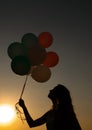 Silhouette of young woman with flying balloons against the sky. Royalty Free Stock Photo