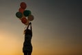 Silhouette of young woman with flying balloons against the sky. Royalty Free Stock Photo