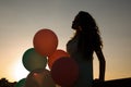 Silhouette of young woman with flying balloons against the sky. Royalty Free Stock Photo