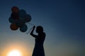 Silhouette of young woman with flying balloons against the sky. Royalty Free Stock Photo