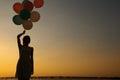 Silhouette of young woman with flying balloons against the sky. Royalty Free Stock Photo