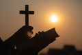 Silhouette of Young woman hands holding holy Bible and lift of christian cross, religion symbol in light and landscape over a Royalty Free Stock Photo