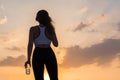 Silhouette young woman in the headphones in the sport clothes with bottle of clear mineral water on the sunset sky backgrounds. Royalty Free Stock Photo