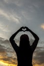 Silhouette of young woman with her hands raised above her head makes a heart-shaped symbol against a beautiful twilight sky Royalty Free Stock Photo