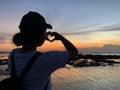 Silhouette of a young woman making heart love sign against colorful sunset on the beach. Showing love and kindness concept. Royalty Free Stock Photo