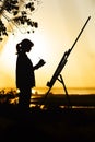 Silhouette of a young woman painting a picture with paints on canvas on an easel outdoors, girl profile engaged in art at sunset