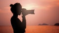 Silhouette of young woman photographer, taking pictures of landscape at sunset Royalty Free Stock Photo