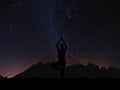 Silhouette young woman practicing yoga pose at night under sky full of stars with colorful milky way