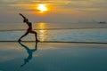 Silhouette young woman practicing yoga on swimming pool and the beach at sunset. Royalty Free Stock Photo